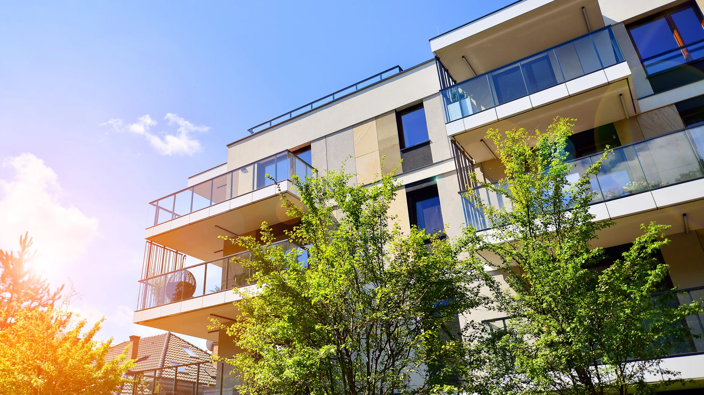 Modern multifamily rental building with glass balconies surrounded by trees